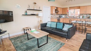 A modern living room with a black leather sofa, a wooden coffee table, and a green patterned rug. - The Shieling (Morpeth)