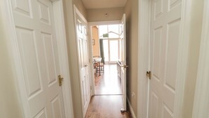 A hallway with white doors, wooden flooring, and a view into a dining area with a table and chairs. - The Shieling (Morpeth)