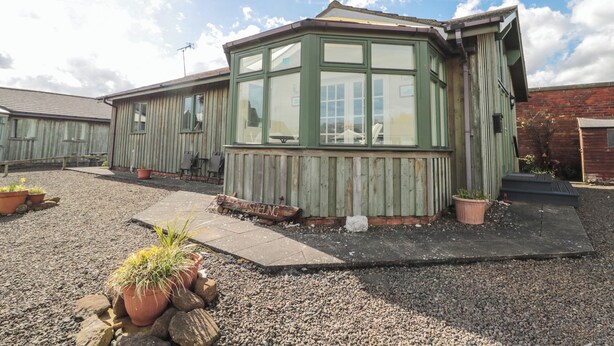 A rustic building with a green window, wooden siding, and a gravel driveway. - The Shieling (Morpeth)