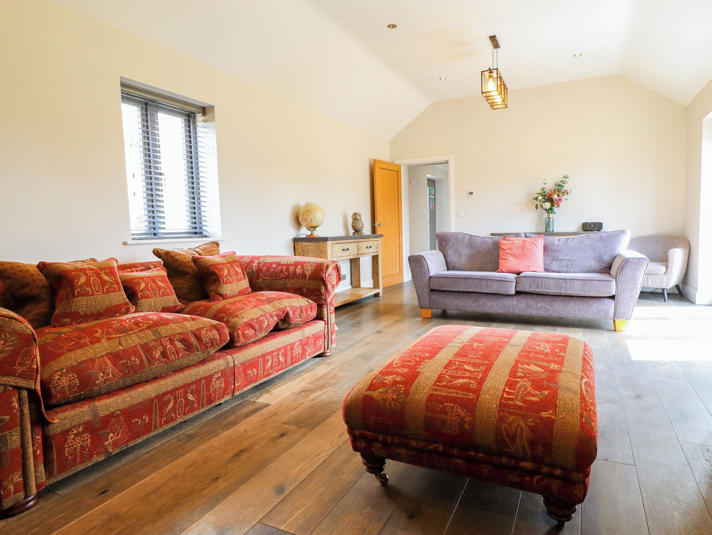 A spacious living room with a large sofa, a smaller sofa, and an ottoman, all arranged on a wooden floor.