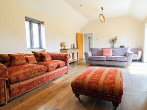 A spacious living room with a large sofa, a smaller sofa, and an ottoman, all arranged on a wooden floor.