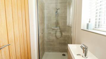 A bathroom with a glass-enclosed shower, a white sink with a chrome faucet, and a window with blinds.