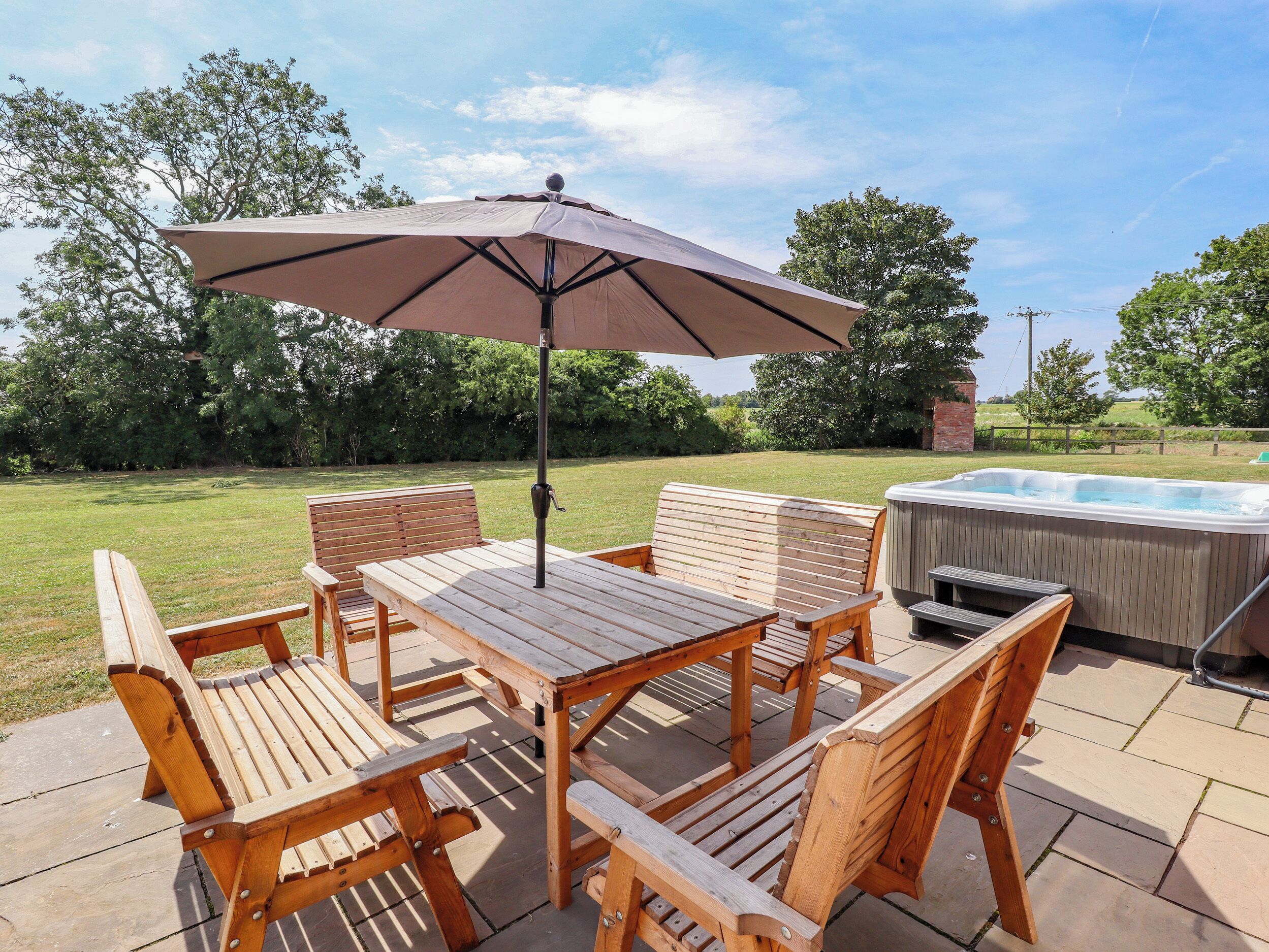 Un patio exterior con muebles de madera, un jacuzzi y una sombrilla grande.