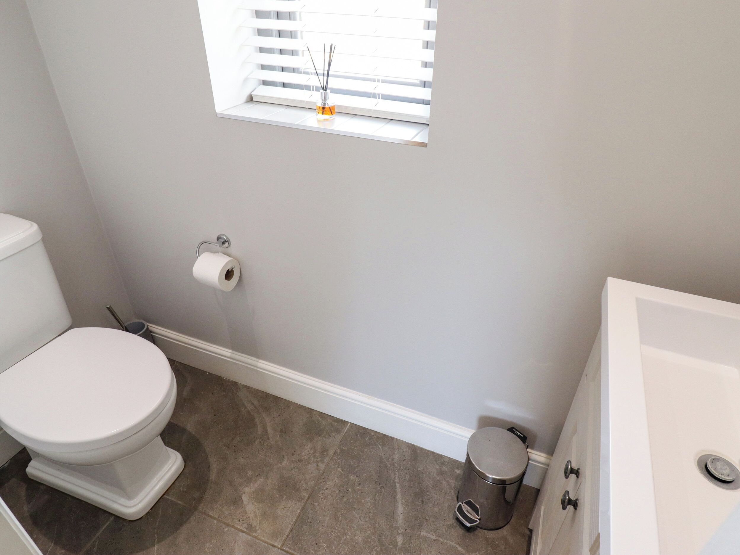 A bathroom with a toilet, a window with a window blind, a trash can, and a bathtub.