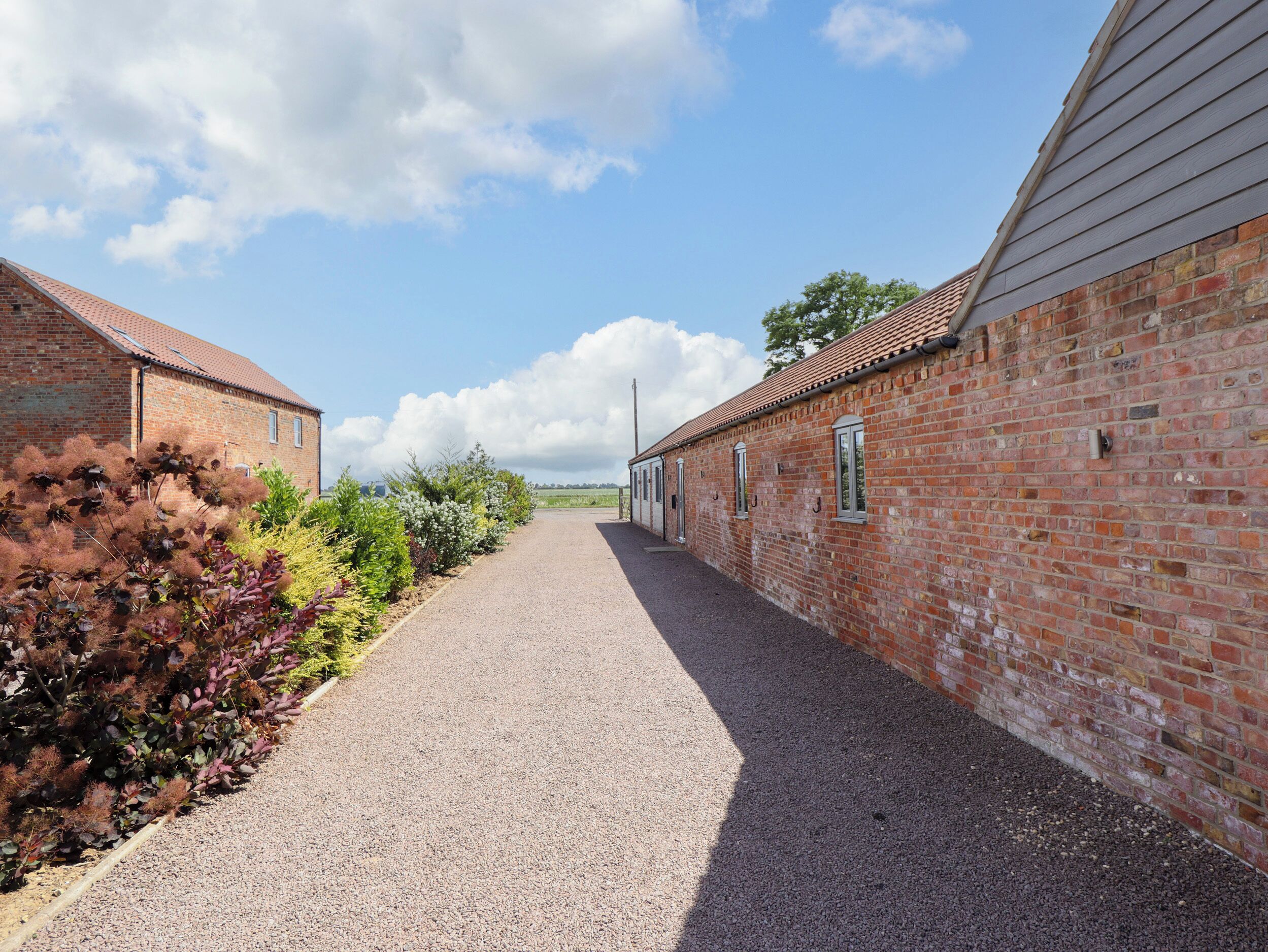 A gravel pathway leading to a row of brick buildings with windows and doors.