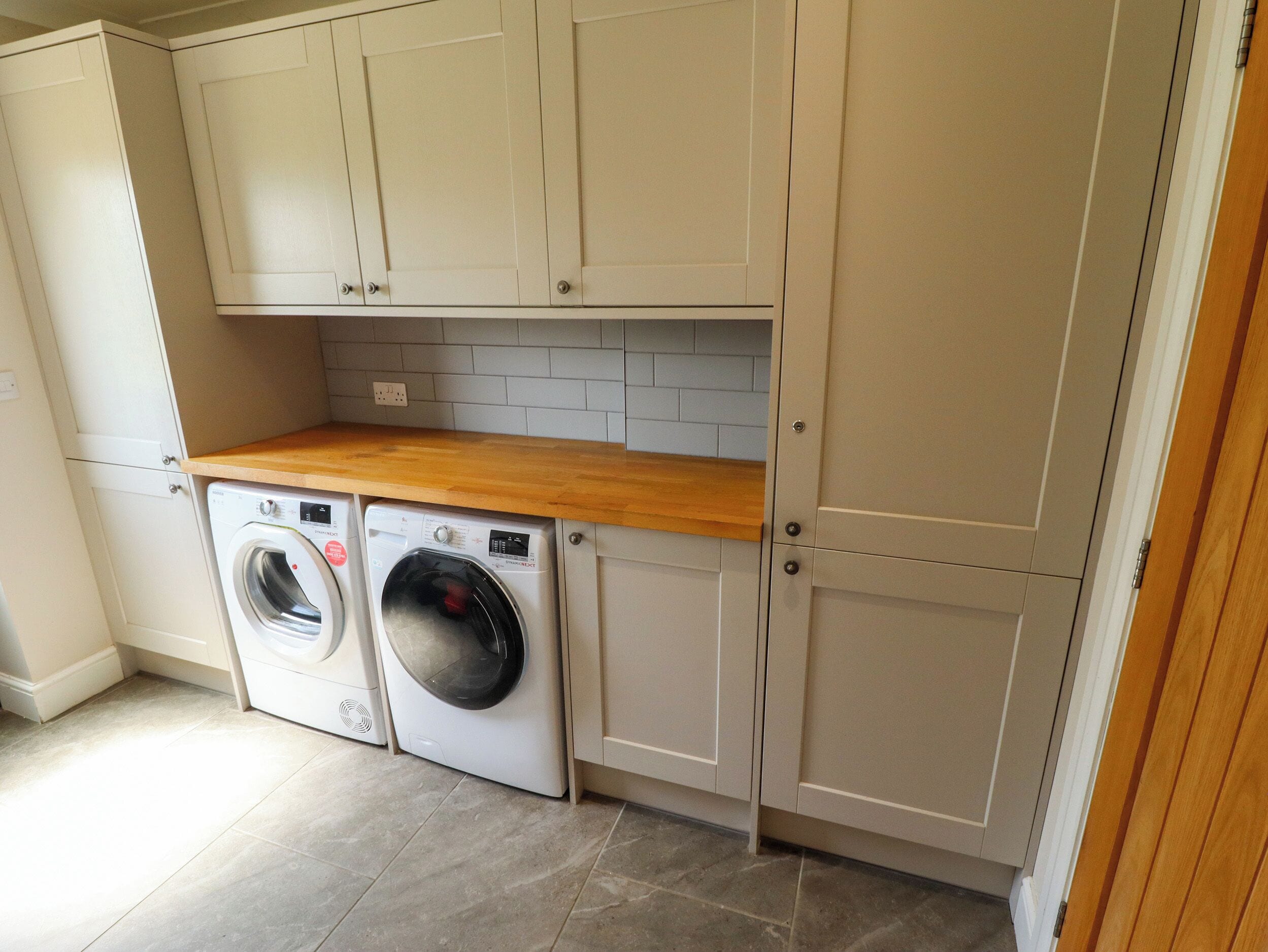A laundry room with a washing machine and dryer, wooden countertop, and light-colored cabinets.