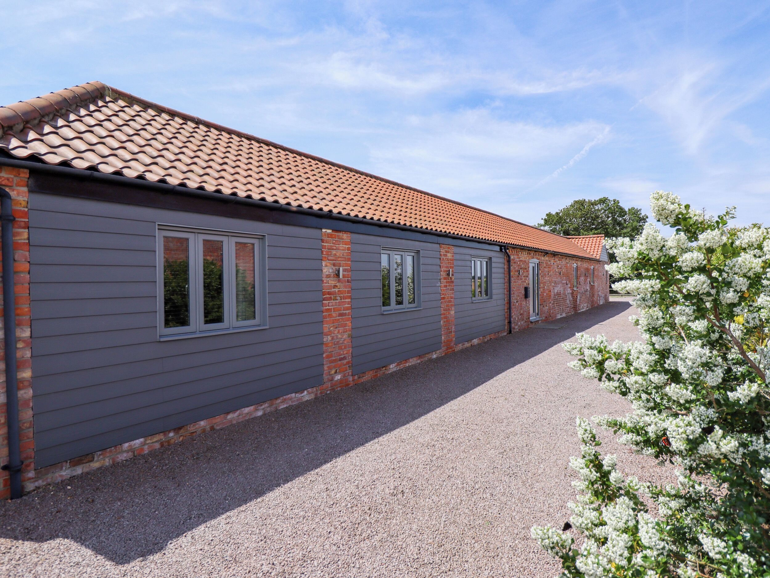 A building with a grey exterior and red-tiled roof, featuring multiple windows and a gravel driveway.