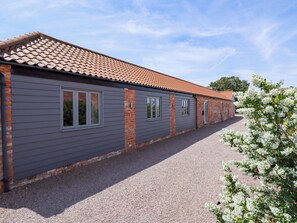 A building with a grey exterior and red-tiled roof, featuring multiple windows and a gravel driveway.
