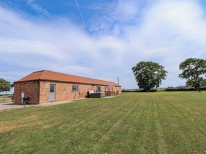 A brick building with a tiled roof, a lawn, and a large tree.