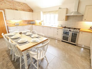 A kitchen with white cabinets, a wooden countertop, and a dining table set for six. - The Stables (Boston)
