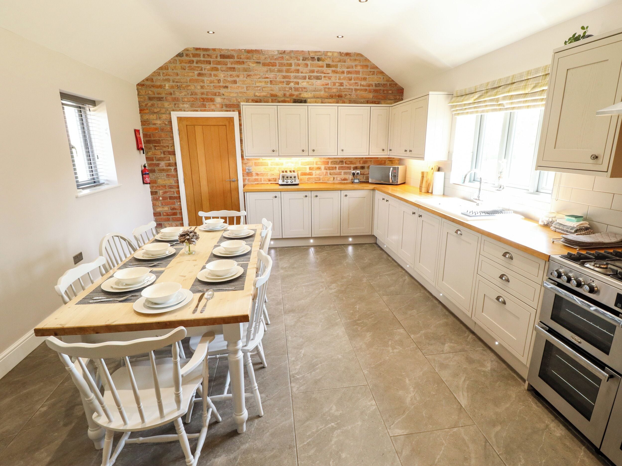 A kitchen with a brick wall, white cabinets, a dining table set for six, and a built-in oven.