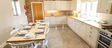 A kitchen with a brick wall, white cabinets, a dining table set for six, and a built-in oven.