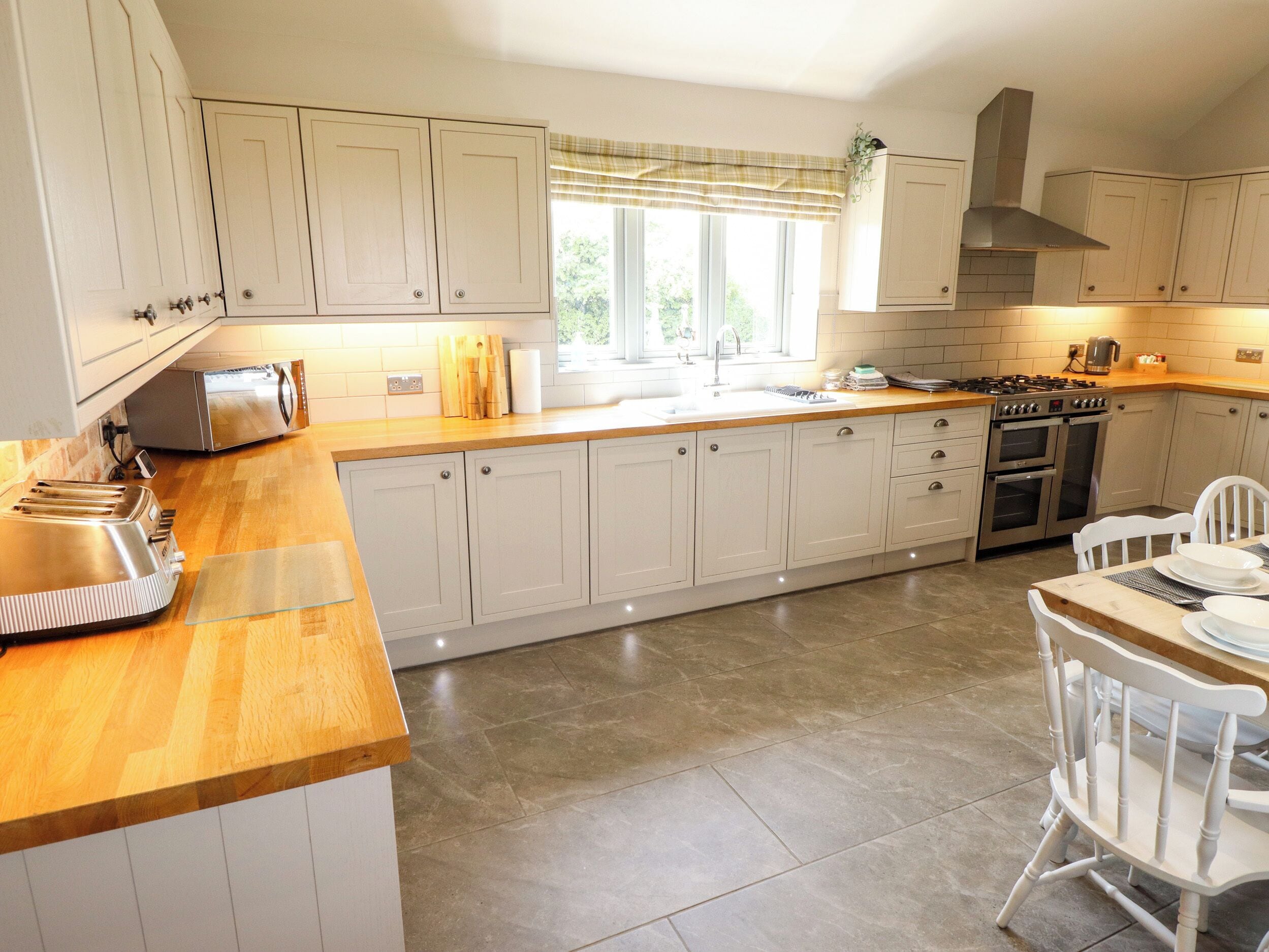 Una cocina con armarios blancos, encimera de madera, estufa y lavaplatos.