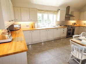 Una cocina con armarios blancos, encimera de madera, estufa y lavaplatos.