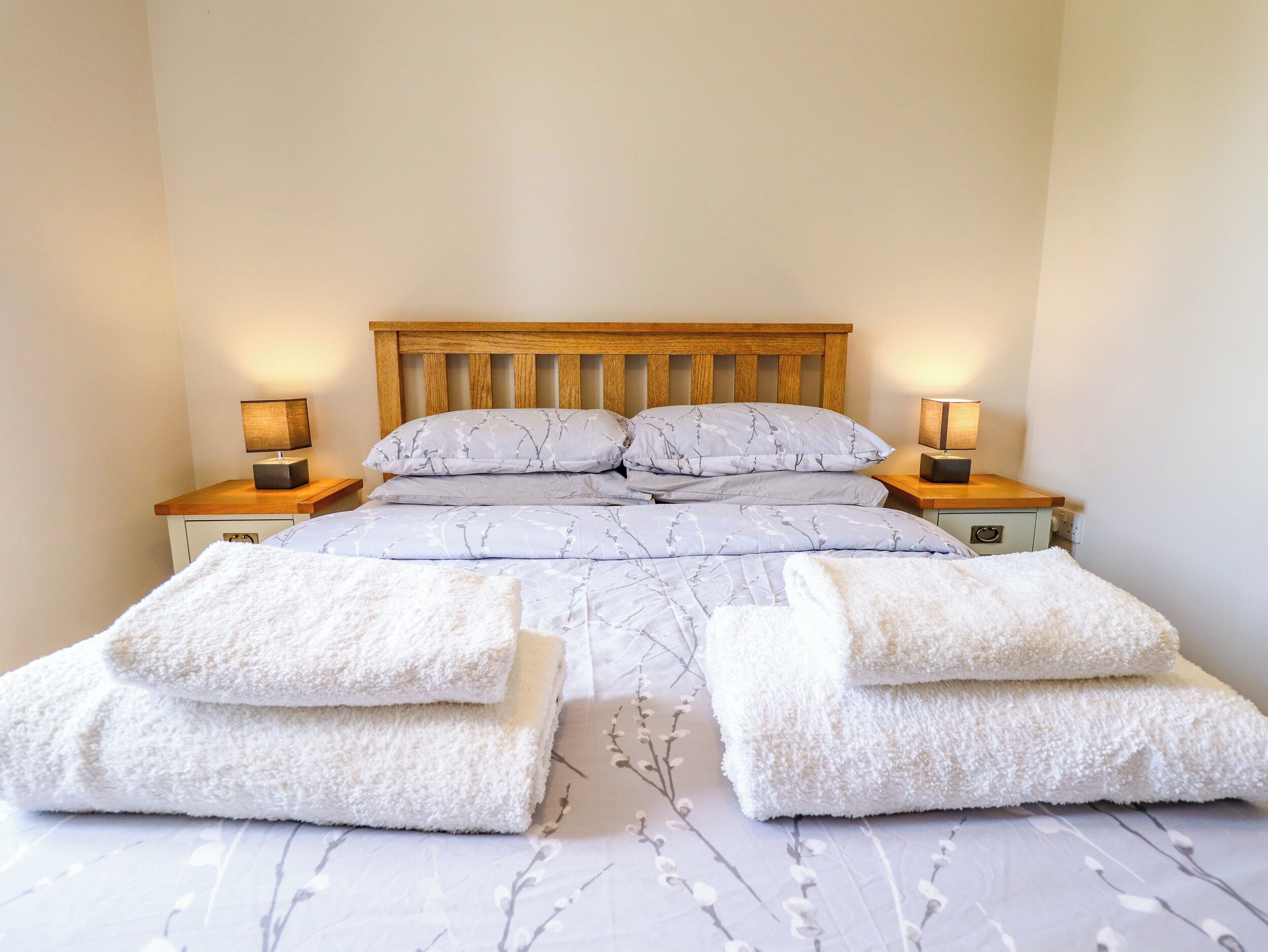 A neatly made bed with a wooden headboard, two bedside tables with lamps, and two folded towels on the bed.