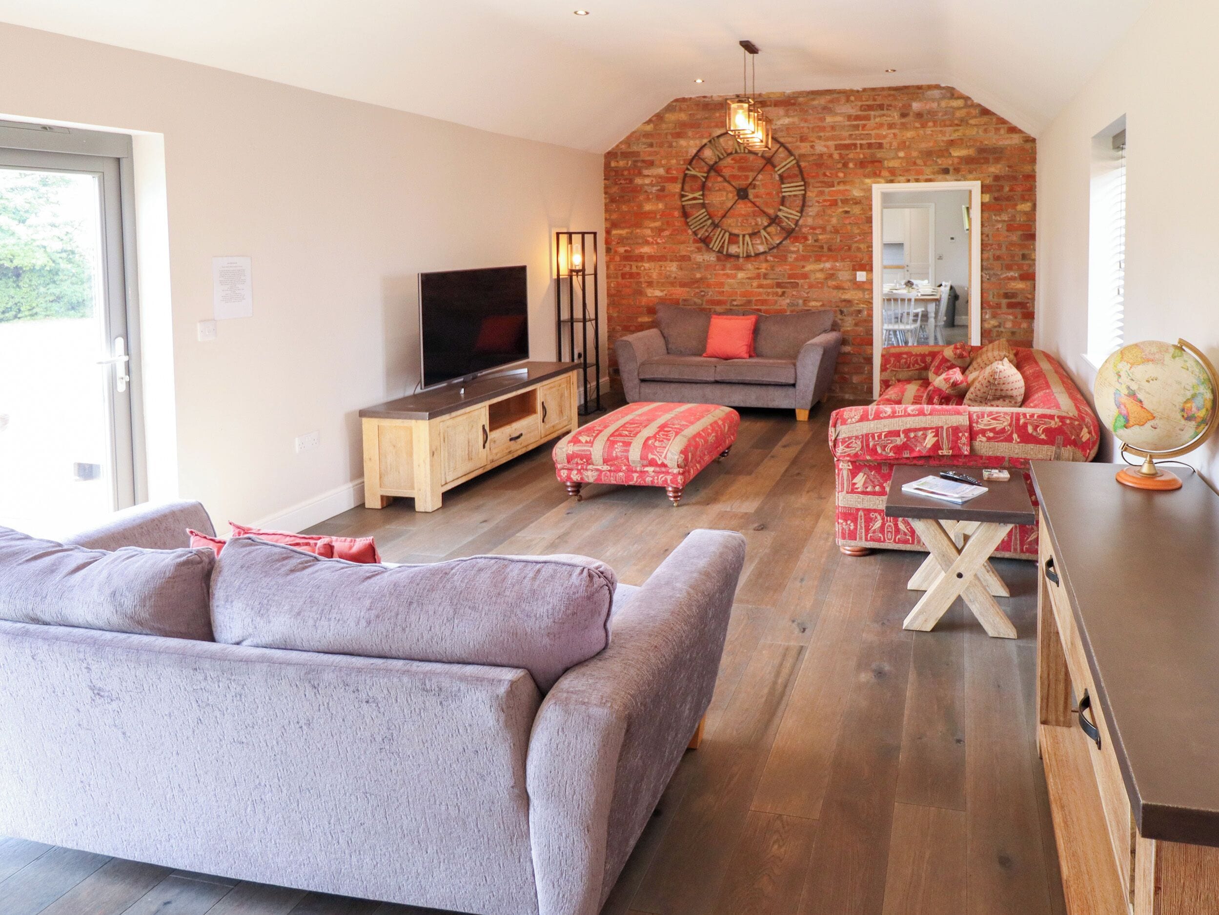 A living room with a television, sofa, ottoman, and a brick wall.