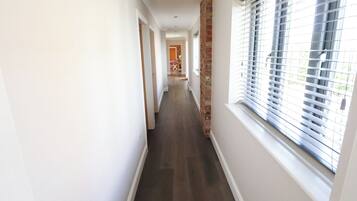 A long, narrow hallway with a wooden floor, white walls, and a brick column.