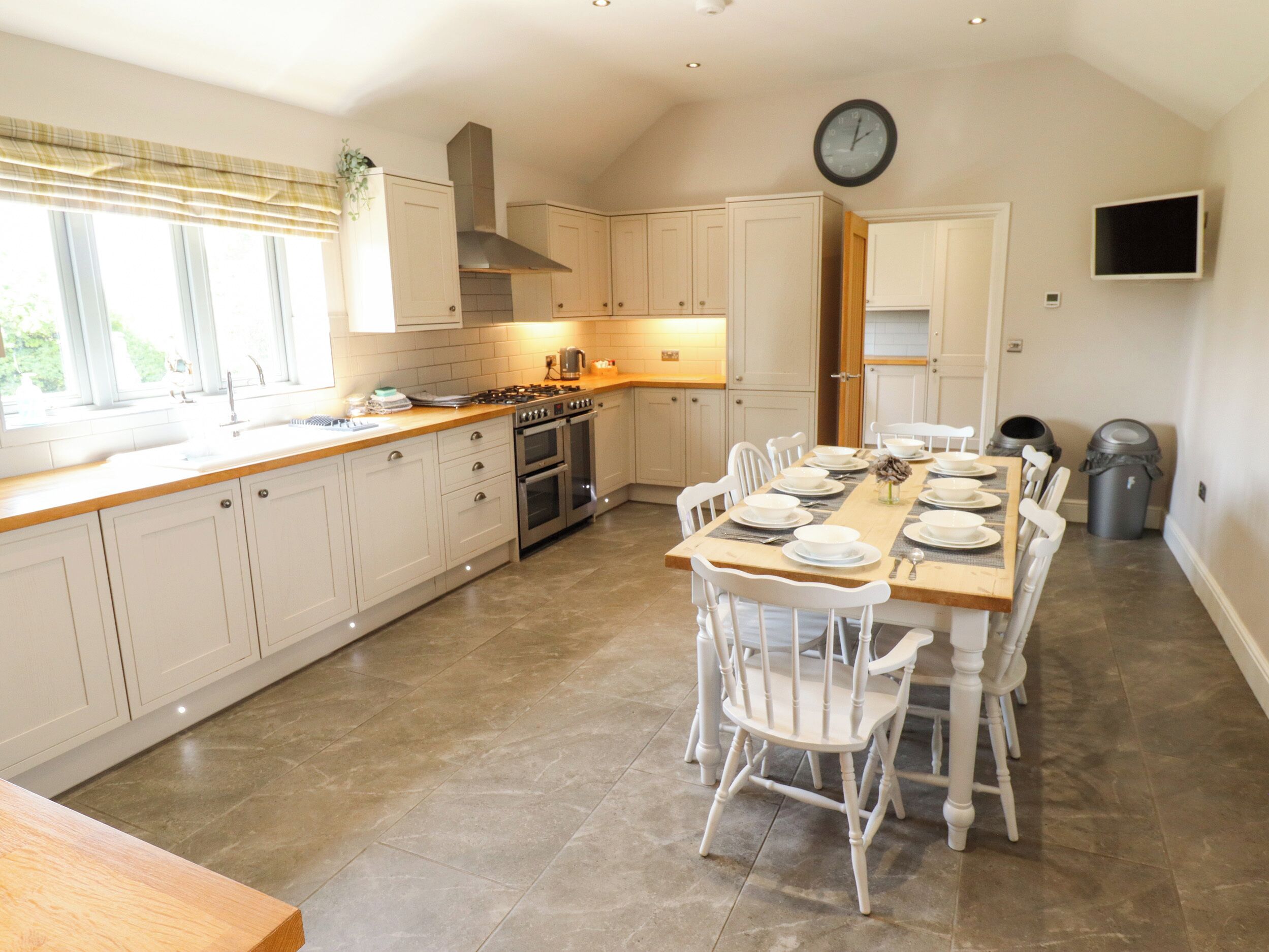 A spacious kitchen with white cabinetry, a dining area with a wooden table and chairs, and a clock on the wall.