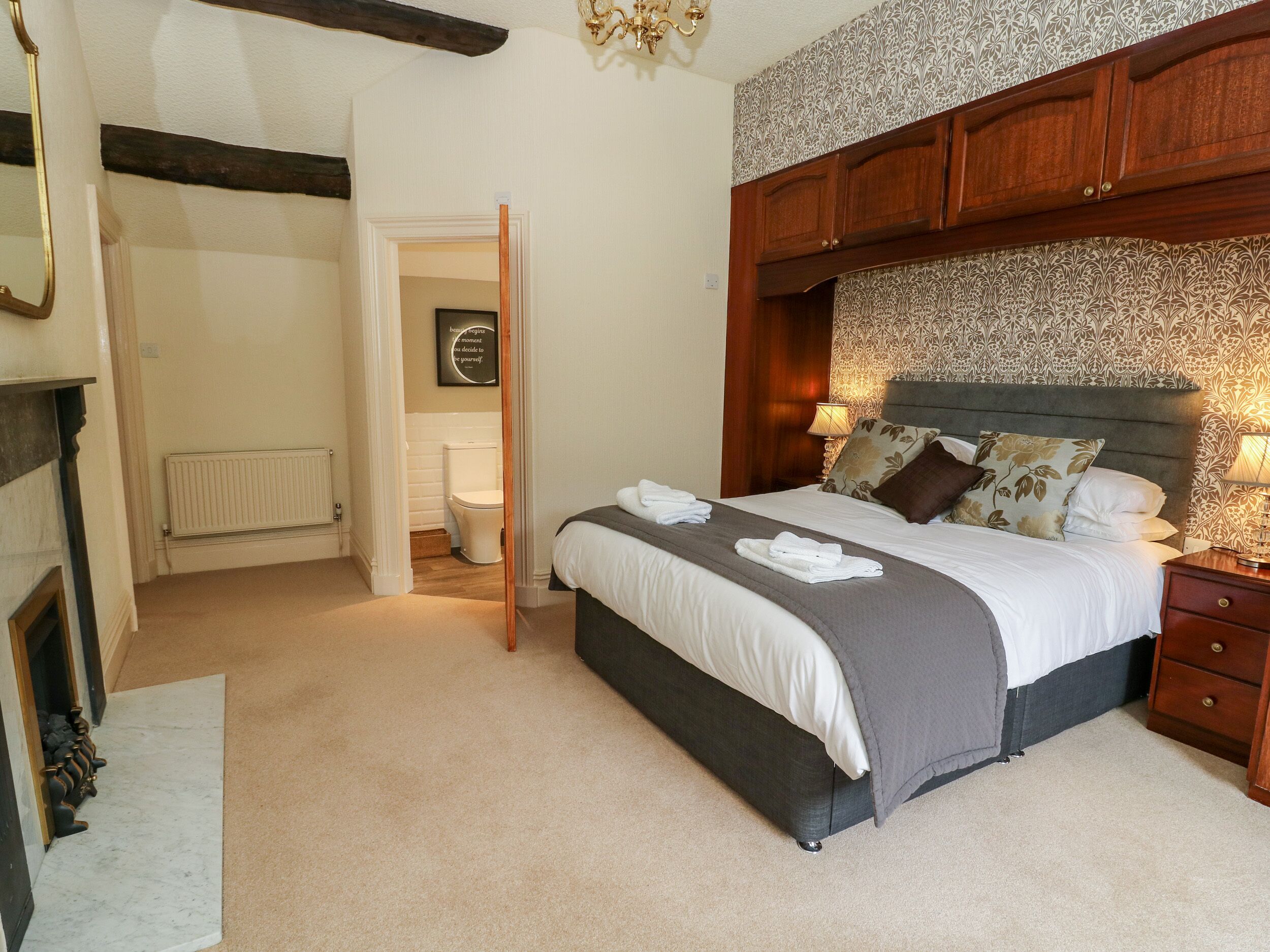 A bedroom with a bed, bedside tables, a radiator, a door leading to another room, and a chandelier.