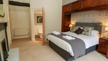 A bedroom with a bed, bedside tables, a radiator, a door leading to another room, and a chandelier.