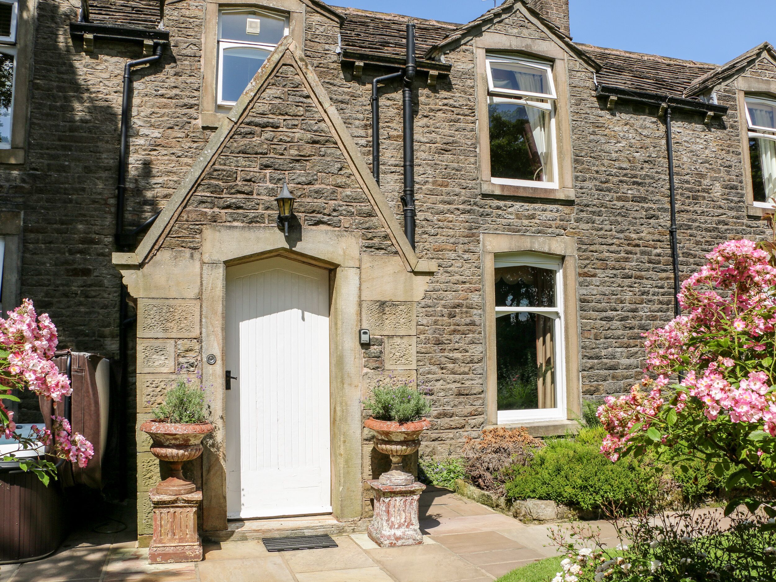 A stone house with a white door, multiple windows, and a small garden with pink flowers.