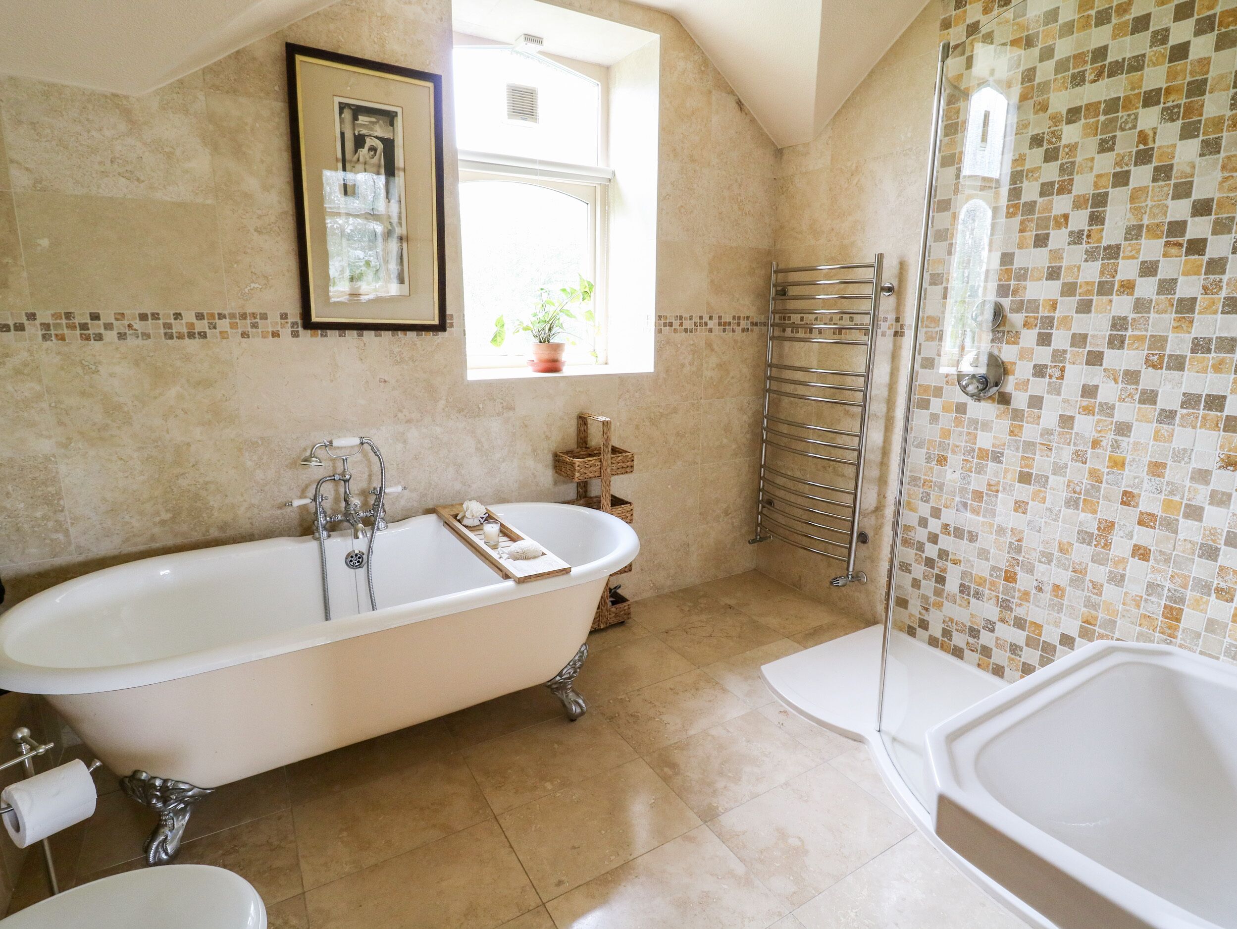 A bathroom with a freestanding bathtub, a shower, and a toilet. There is a window with a view of greenery outside.