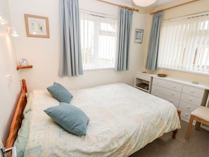 Une chambre à coucher avec un lit, une commode, une chaise et une fenêtre avec des rideaux.