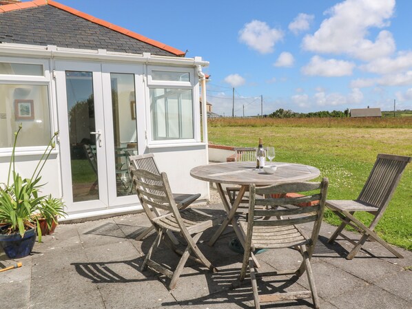A patio with a round table and two wooden chairs, a bottle of wine, and a glass on the table.