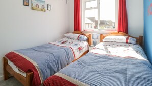 Een slaapkamer met twee eenpersoonsbedden, een raam met rode gordijnen en uitzicht op gebouwen.