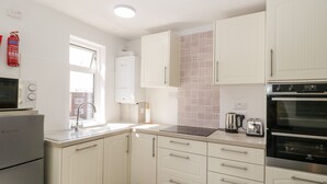 A modern kitchen with white cabinets, a built-in oven, a microwave, and a kettle.