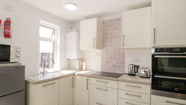 Een moderne keuken met witte kastjes, een inbouwoven, een magnetron en een waterkoker.
