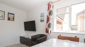 Een kamer met een wandgemonteerde flatscreen-tv, een eettafel met een tafelkleed met een patroon, en een raam met uitzicht op gebouwen.