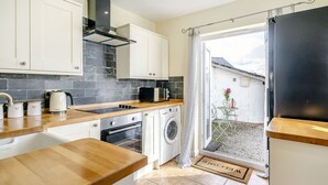 A compact kitchen with a wooden countertop, a built-in oven, a washing machine, and a black range hood. - Kidsty Cottage (Penrith)
