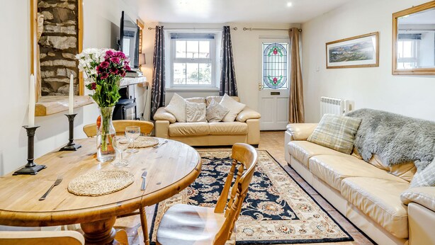 A cozy living room with a dining table, two sofas, a stone wall, and a stained glass window. - Kidsty Cottage (Penrith)