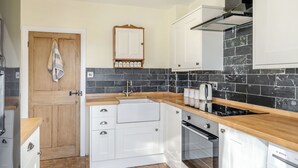 A modern kitchen with white cabinets, a black tiled backsplash, and a Bosch oven. - Kidsty Cottage (Penrith)