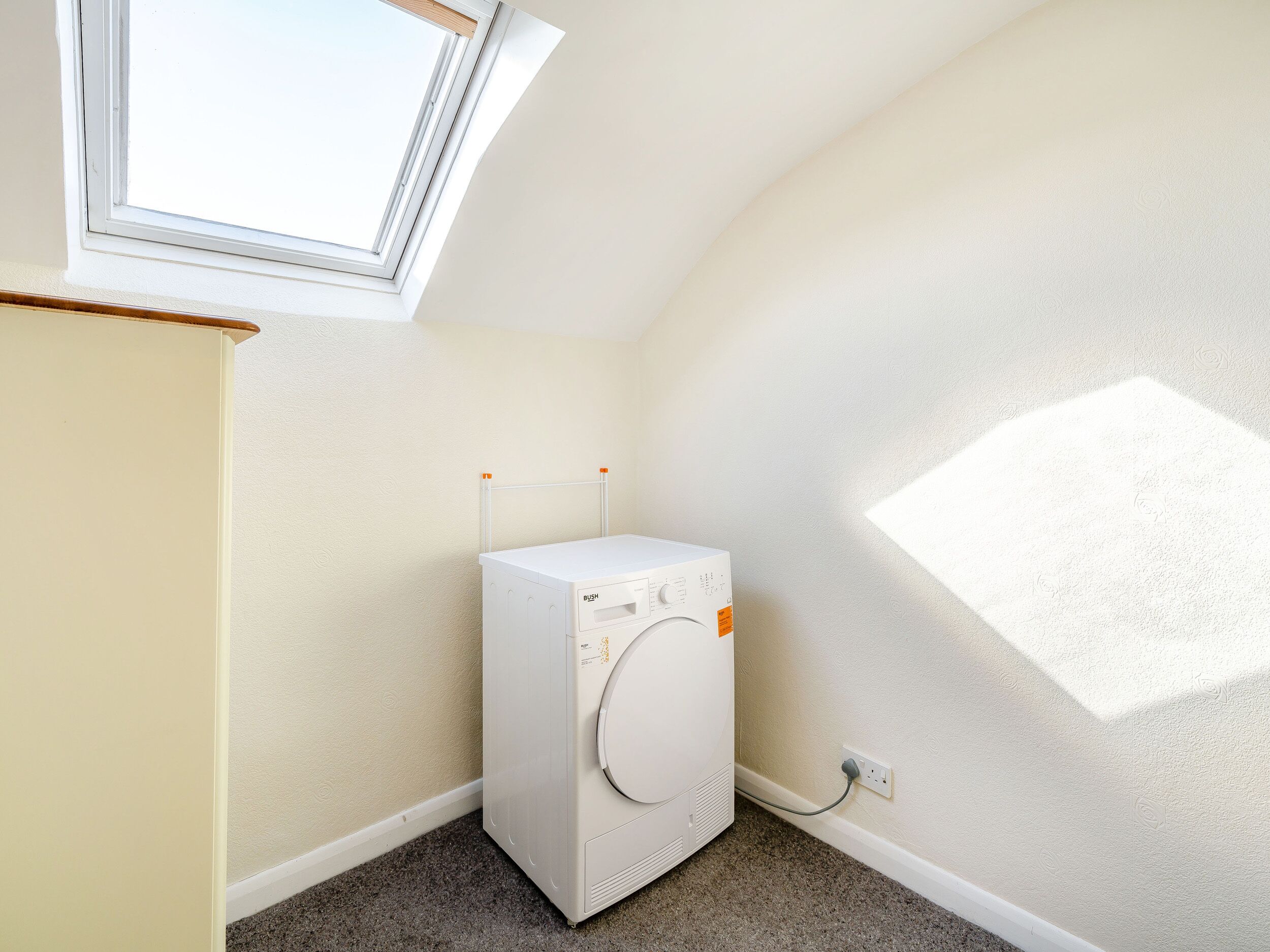 A laundry room with a white washing machine, a small window, and a power outlet on the wall.