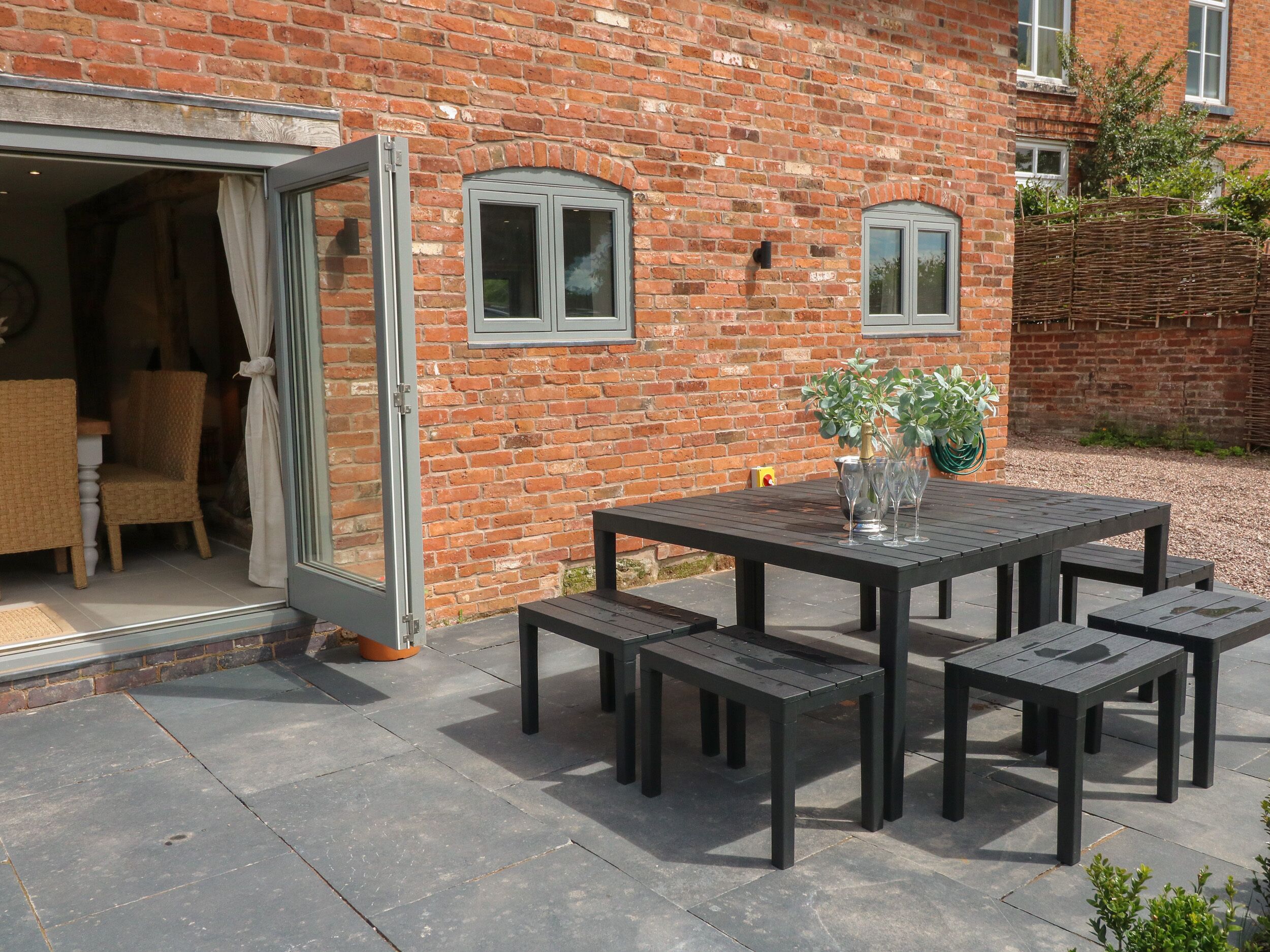 Een terras met een zwarte tafel en stoelen, een rieten stoel en een potplant.