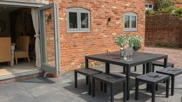 Een terras met een zwarte tafel en stoelen, een rieten stoel en een potplant.