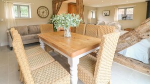 Un comedor con mesa de madera y sillas tejidas, un sofá y una gran planta como adorno central.