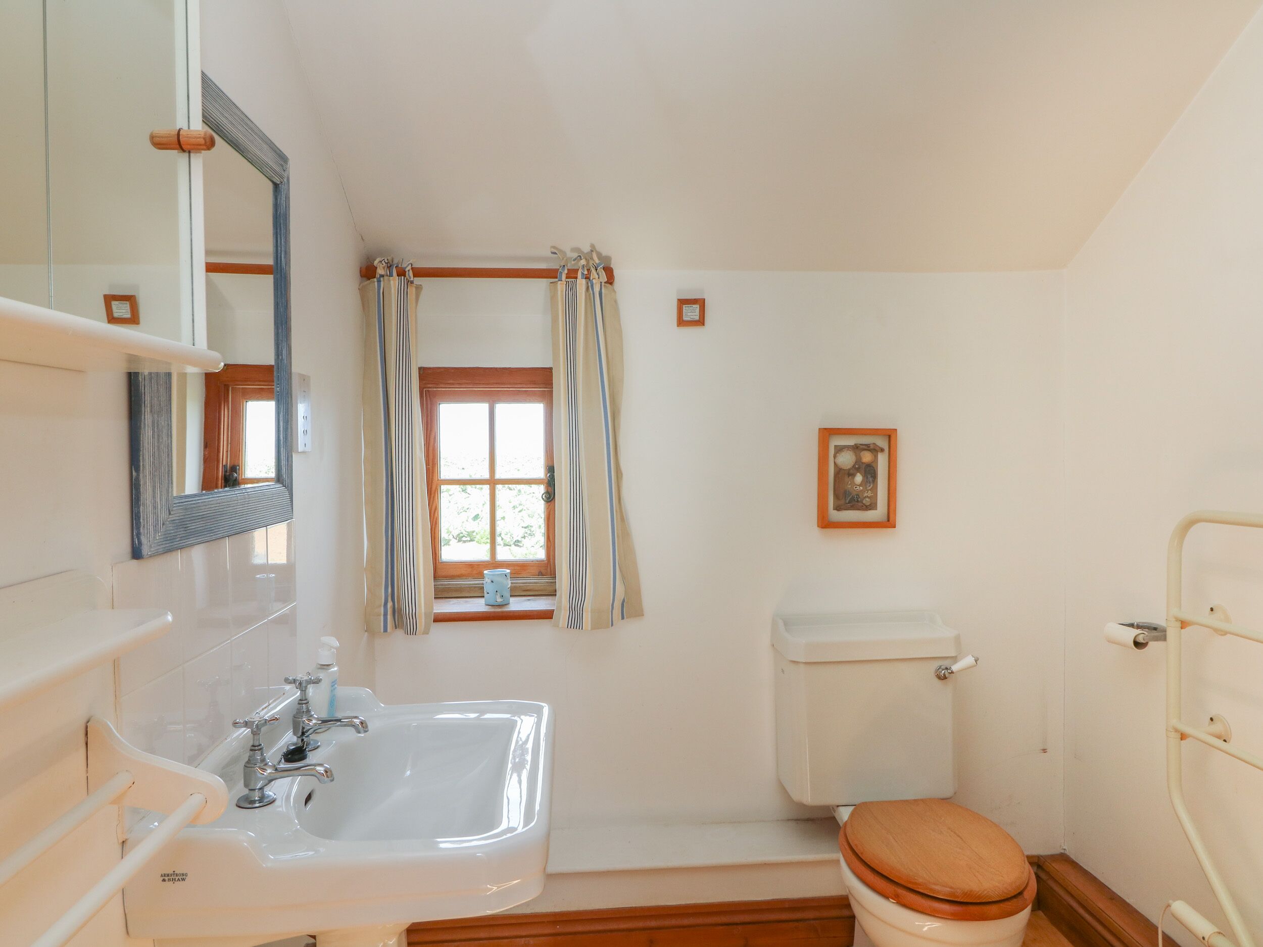 A bathroom with a white sink, a toilet, a shower, and a window with curtains.