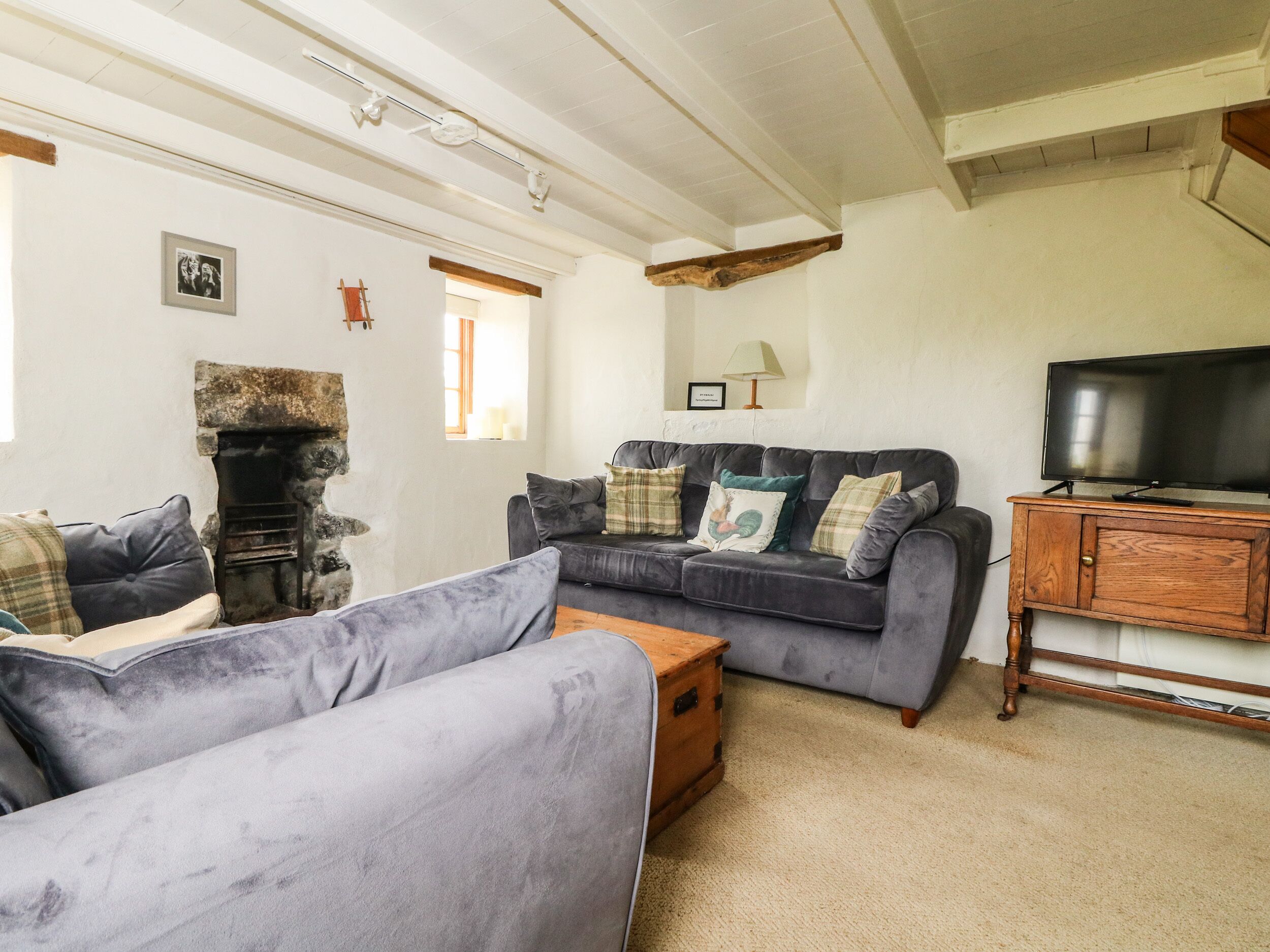 A cozy living room with a fireplace, a grey sofa set, a wooden cabinet with a television, and a stone wall.