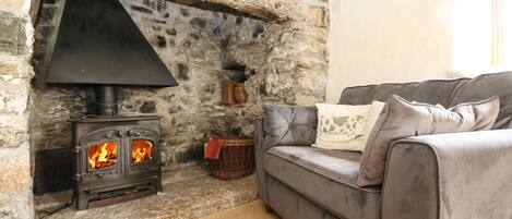 A stone fireplace with a black stove, a grey sofa with cushions, and a wicker basket.