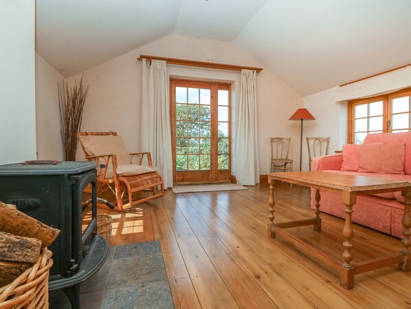 A cozy room with a wooden floor, a sofa, a table, a chair, and a fireplace. - Higher Roskorwell Cottage (Helston)