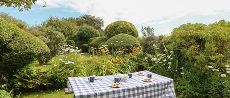 A picnic table set up in a lush garden with a checkered tablecloth, surrounded by various plants and flowers.
