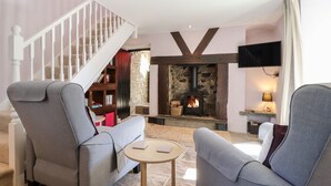 A living room with two grey armchairs, a small round table, a stone fireplace, a television, and a staircase. - Morawel Fach (Newport)