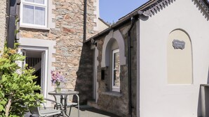 A stone building with a small patio area, a table with chairs, and a flower vase. - Morawel Fach (Newport)