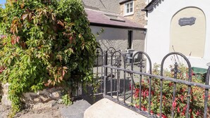 A residential property with a stone facade, a metal gate, and a small garden with red flowers. - Morawel Fach (Newport)