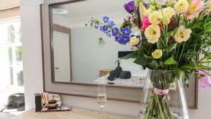 Een slaapkamer met een grote spiegel, een nachtkastje met een glas water en een bloevas.