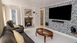 Un soggiorno con camino, un divano in pelle nera, un tavolino da caffè in vetro e una TV a parete.