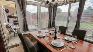 Zona pranzo con tavolo in legno apparecchiato per quattro persone, circondato da sedie e vista su un giardino attraverso ampie finestre.